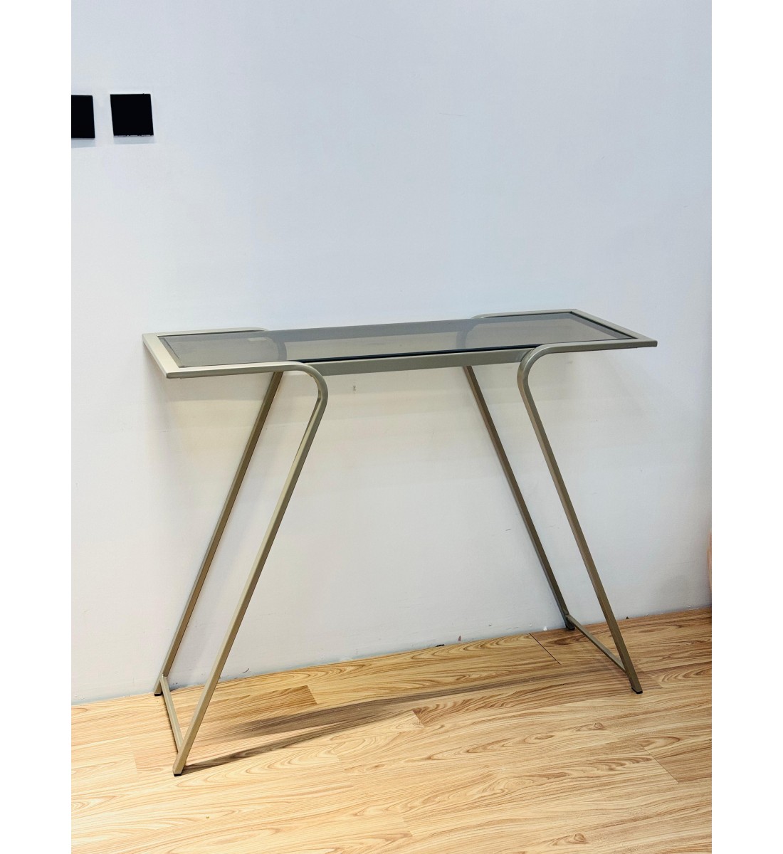 طاولة مدخل عصرية بتصميم انسيابي يجمع بين الزجاج الشفاف المائل للدخاني والإطار المعدني الذهبي الفاتح المتين 110×34×90سم طاولة مدخل عصرية بتصميم انسيابي يجمع بين الزجاج الشفاف المائل للدخاني والإطار المعدني الذهبي الفاتح المتين 110×34×90سم