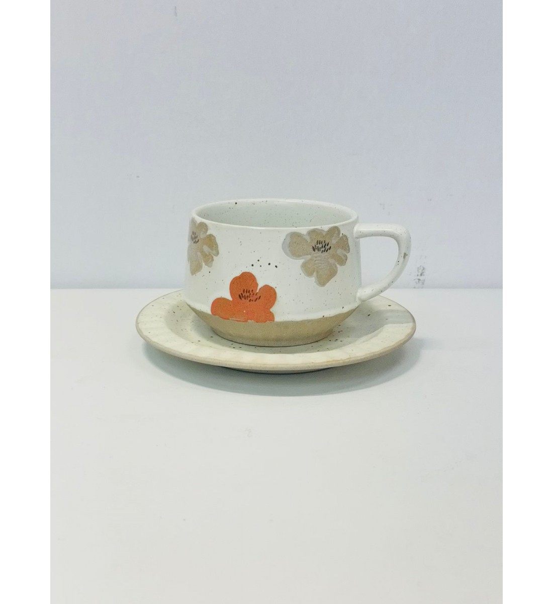 هذا طقم أنيق مكوّن من فنجان وصحن خزفي بتصميم يدوي مميز.لقطعة باللون الأبيض المائل للكريمي مع نقاط صغيرة متناثرة بالرمادي