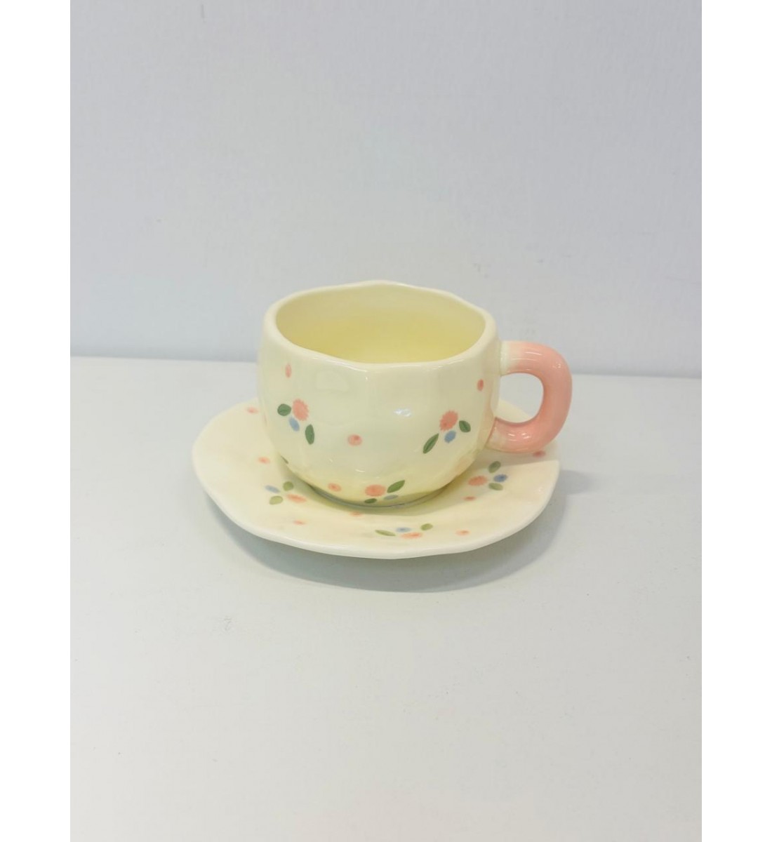 هذا طقم خزفي جميل مكوّن من فنجان وصحن بتصميم ناعم ومرح يأتي باللون الكريمي الفاتح مع رسومات صغيرة لزهور متناثرة بألوان وردي، أزرق، وأخضر 