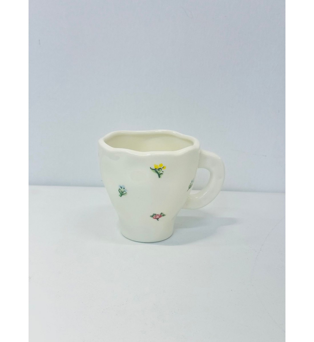 هذا كوب سيراميك أنيق باللون الأبيض العاجي، يتميز بتصميم مزين برسومات زهرية صغيرة بألوان الاصفر الازرق