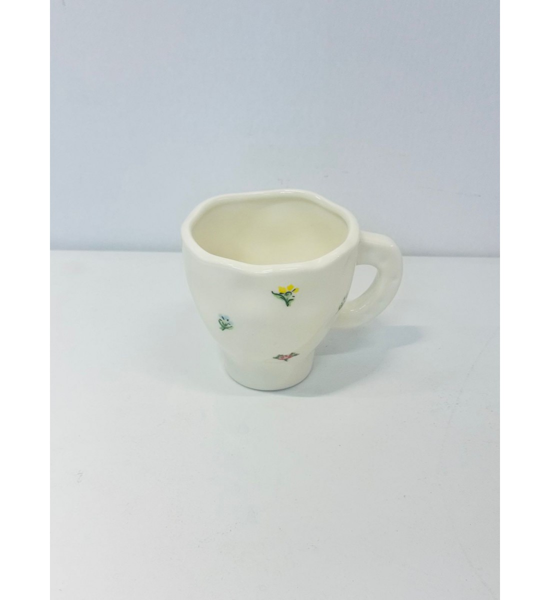 هذا كوب سيراميك أنيق باللون الأبيض العاجي، يتميز بتصميم مزين برسومات زهرية صغيرة بألوان الاصفر الازرق
