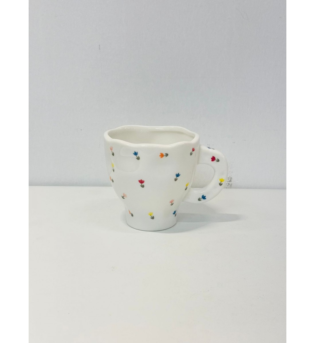 هذا كوب سيراميك أنيق باللون الأبيض العاجي، يتميز بتصميم مزين برسومات زهرية صغيرة بألوان الاصفر الازرق