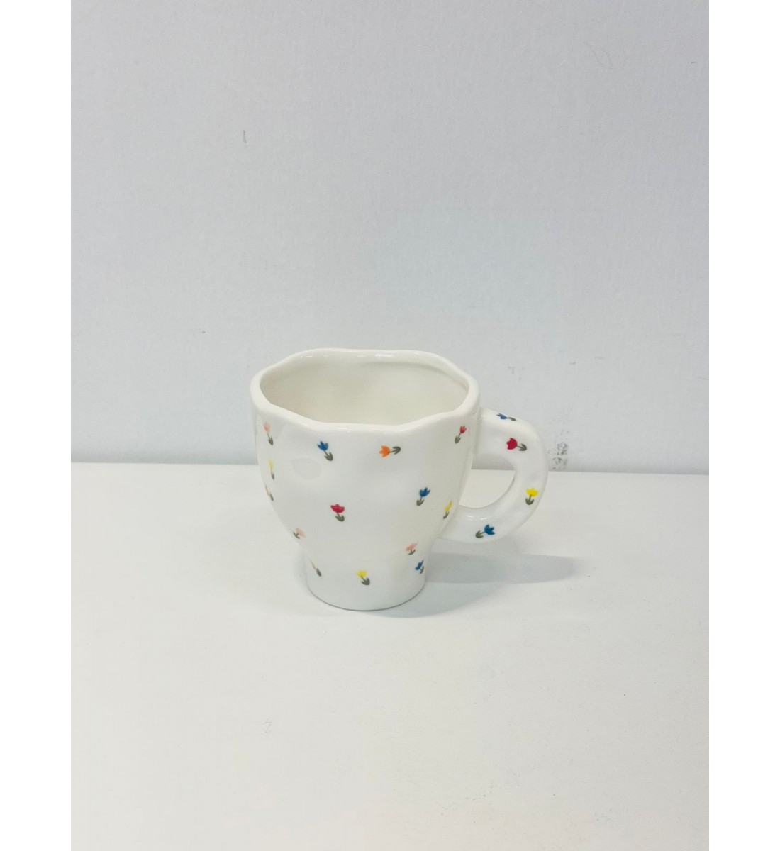 هذا كوب سيراميك أنيق باللون الأبيض العاجي، يتميز بتصميم مزين برسومات زهرية صغيرة بألوان الاصفر الازرق